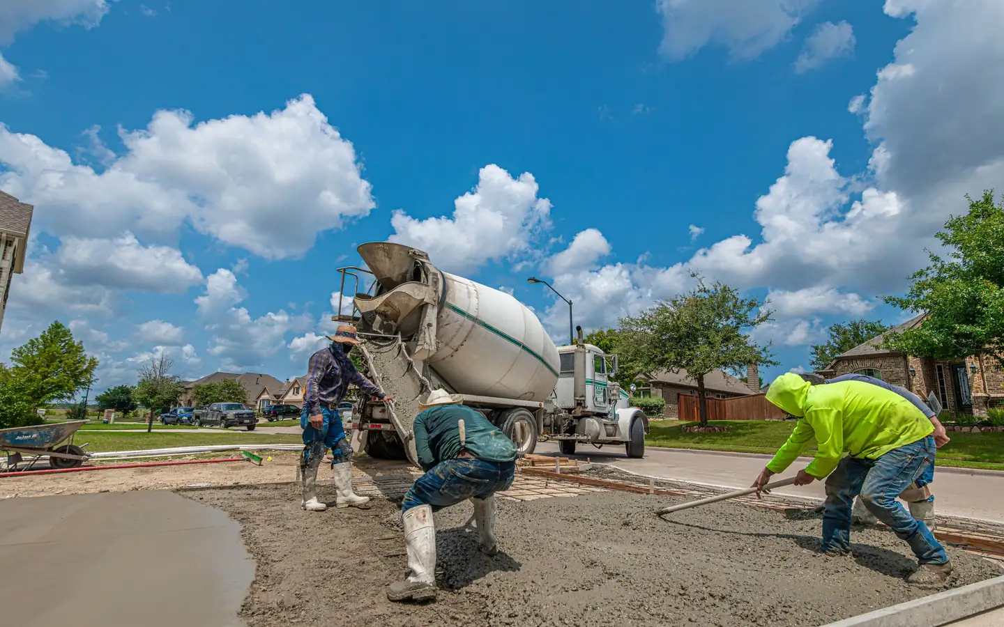 Concrete crew placing a new driveway from a ready-mix truck in a Texas subdivision, one finisher pulling concrete with a come-along